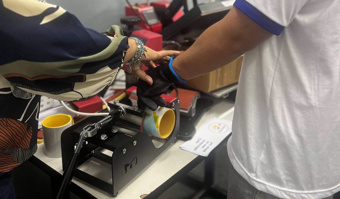 Participante e professora usando a prensa de sublimação para personalizar uma caneca