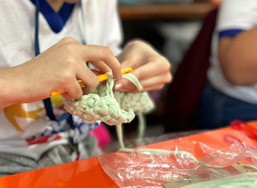 Mãos de uma participante fazendo crochê com fio verde