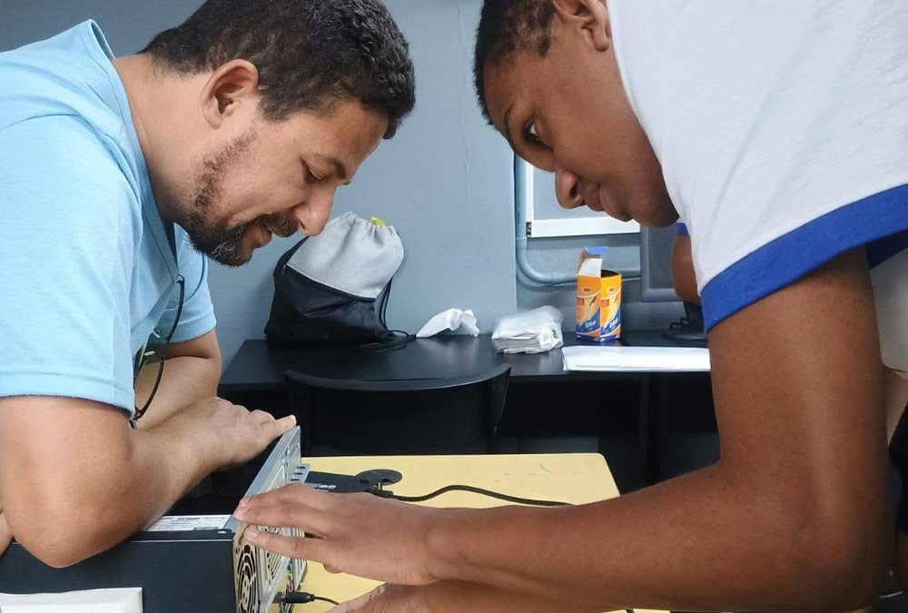 Participante e professor conectando cabos em um computador na aula de Auxiliar de Informática