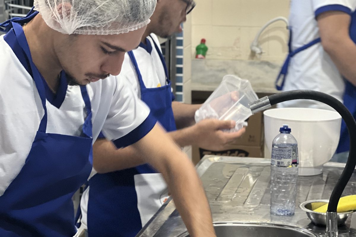 Participantes de touca e avental azul limpando a pia e lavando utensílios na cozinha do Instituto