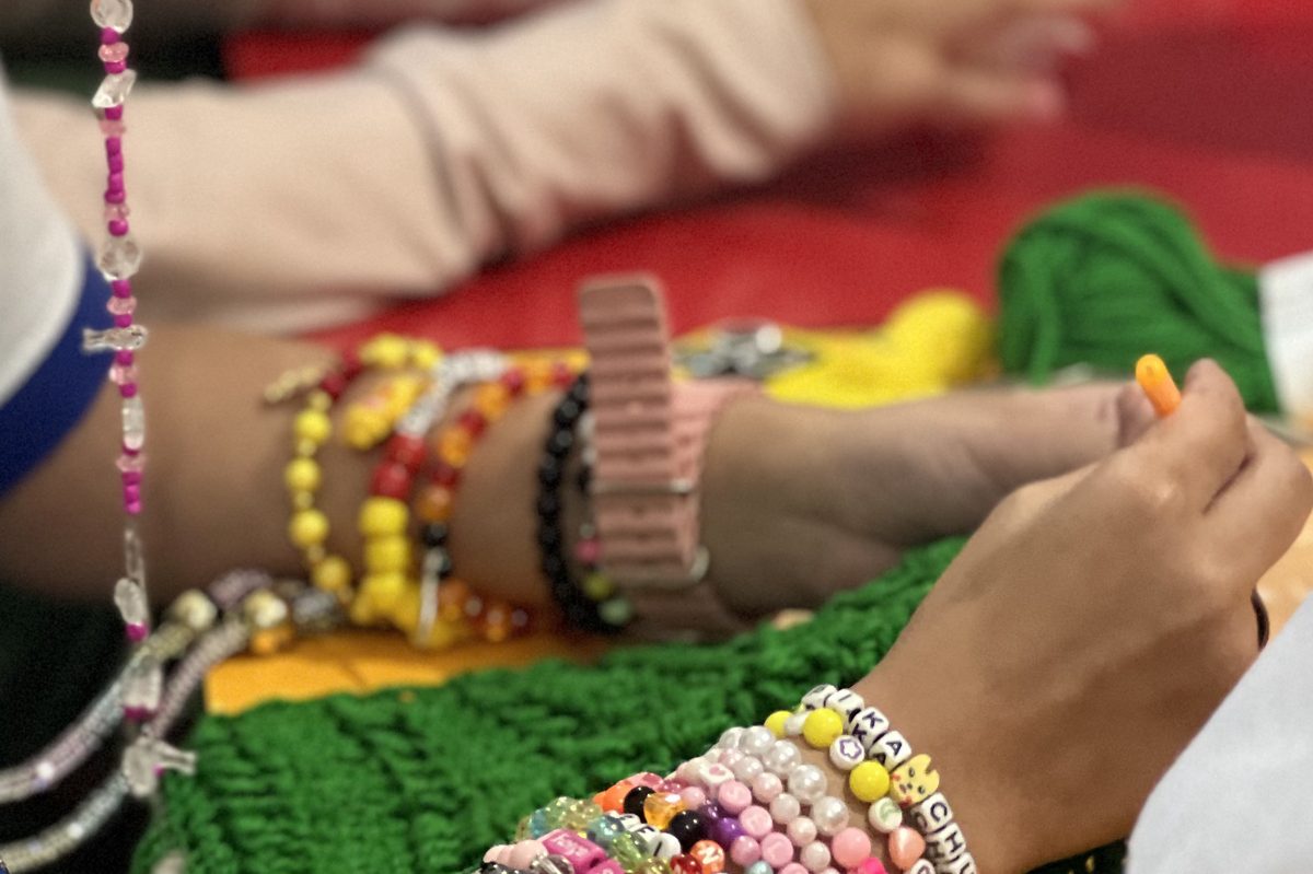 Mãos de uma participante com pulseiras coloridas de miçangas fazendo crochê com fio verde